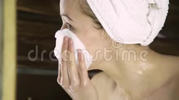 漂亮的女人拿着毛巾用棉垫清洁她的脸女孩从脸上洗掉面具视频的预览图