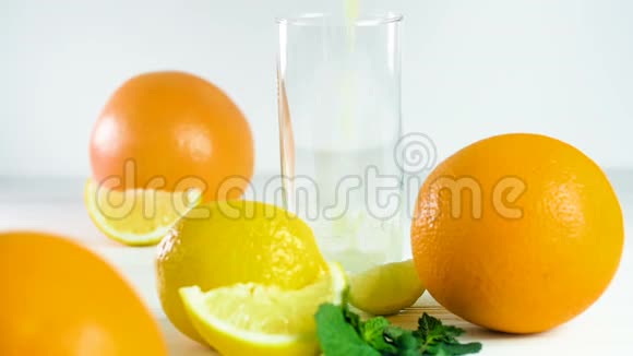 在各种柑橘类水果旁边的白色木桌上用玻璃杯倒入橙汁的慢镜头视频的预览图