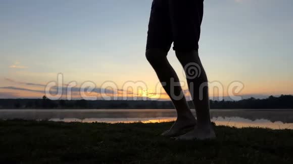 年轻男子的双腿在邋遢的夕阳下沿着湖走视频的预览图