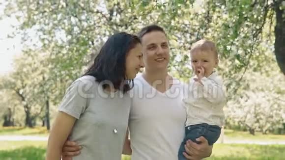 微笑的白种人父母和儿子在夏天的苹果树公园散步视频的预览图