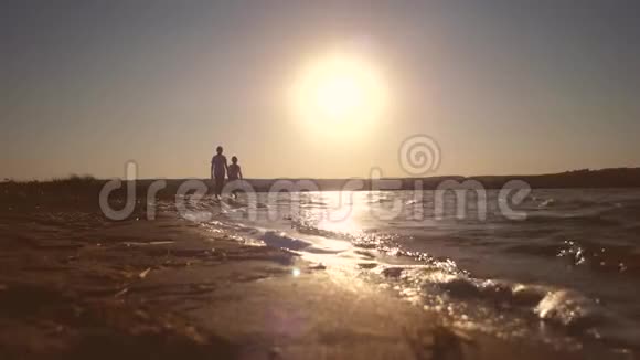 孩子们走在海滩上脚踩在红色傍晚日落的水面上视频的预览图