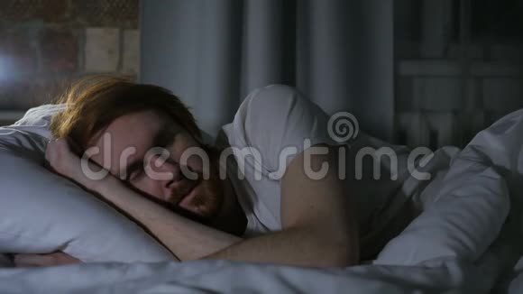 躺在床上睡觉的红发胡子男晚上睡在黑暗的房间里视频的预览图