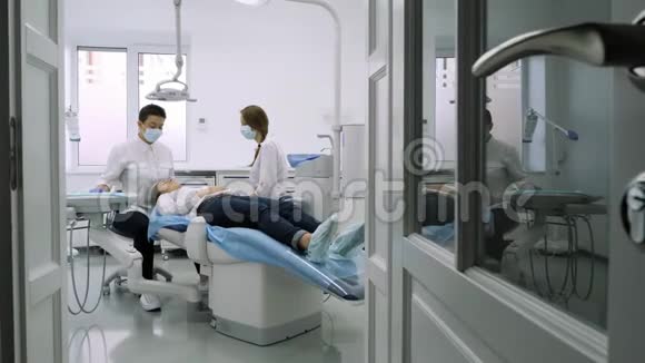 病人坐在蓝色的牙医椅上牙医助理帮助他视频的预览图