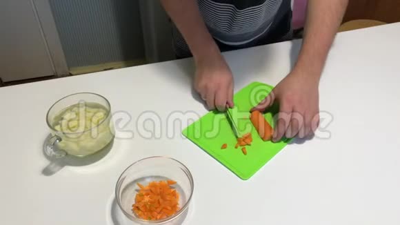 一个人切蔬菜做饭用刀子在切割板上打碎胡萝卜并将其转移到容器中视频的预览图