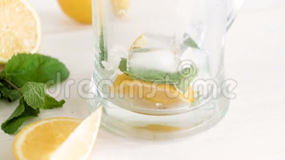 用冰块柠檬和薄荷叶将碳酸水倒入玻璃中的慢镜头准备好柠檬水视频的预览图