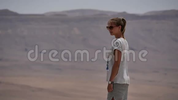 戴墨镜的年轻女子站悬崖边环顾沙漠视频的预览图