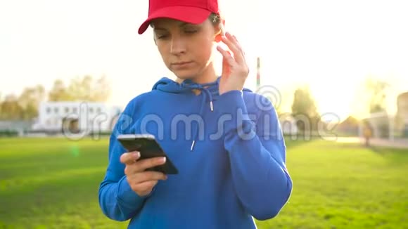 拥有无线耳机和智能手机的女人选择音乐并在日落时穿过体育场慢动作视频的预览图