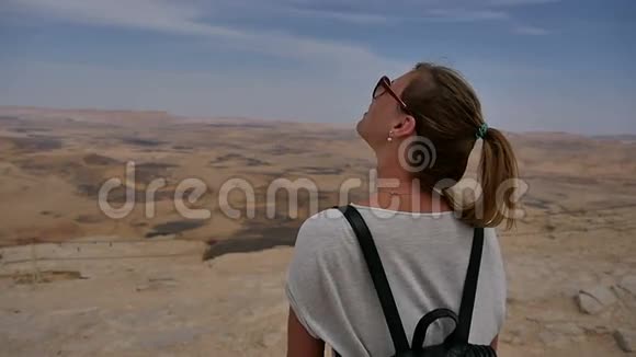 年轻女子背着背包站在悬崖边望着天空转身视频的预览图