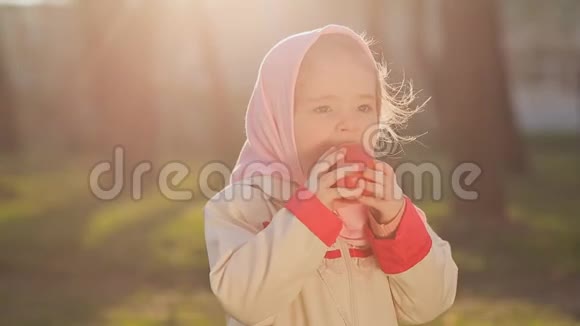 一个穿着粉红色头巾的俄罗斯小女孩在日落时吃红苹果视频的预览图