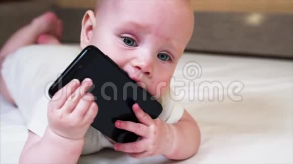 看着相机咀嚼黑色智能手机的男婴肖像视频的预览图