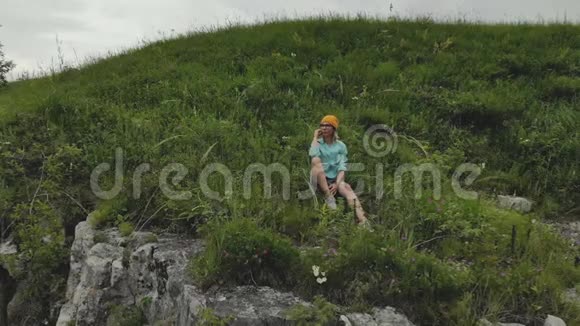 年轻的时髦女人坐在高高的岩石墙上的边缘空中观景无人机缓慢地向后飞行视频的预览图