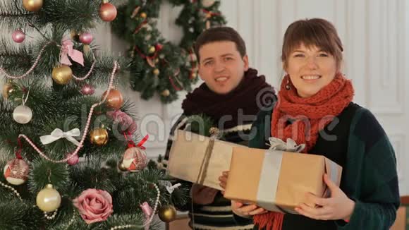 一对美丽的年轻夫妇在新年树附近相爱送给观众礼物圣诞节和新年主题视频的预览图
