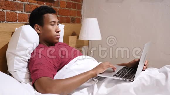 头痛疲惫的非洲男人在床上工作视频的预览图