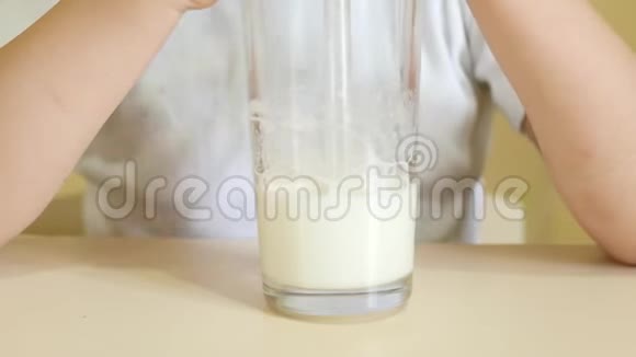 一个孩子通过吸管从杯子里喝牛奶一杯牛奶特写视频的预览图
