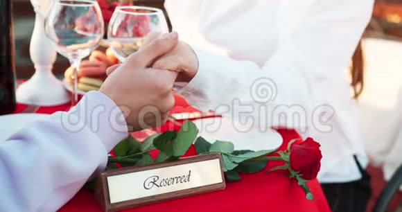 情侣牵手的浪漫户外晚餐桌子上装饰着保留的牌匾和红玫瑰没有脸4k视频的预览图