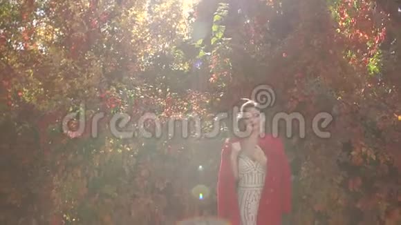 一幅美丽的女孩穿着裙子穿着红色外套在秋天公园里的肖像视频的预览图