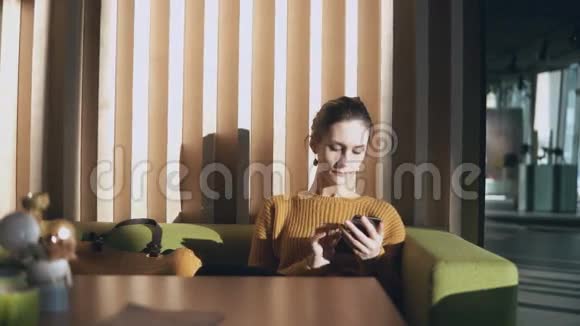 年轻迷人的女人坐在酒店里拿着智能手机女商人在大厅的沙发上上网视频的预览图