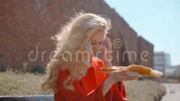 美丽的金发女人正在公园里吃着美味的巨大三明治视频的预览图