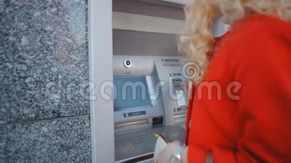 美丽的金发女人把一张银行卡放在街上的自动取款机上视频的预览图