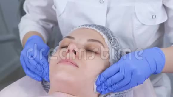 美容师用棉垫擦拭一个年轻女人的脸美容师戴手套和面部特写视频的预览图