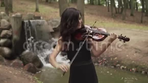 优雅的小提琴手具有灵感穿裙子的女孩在森林里拉小提琴视频的预览图