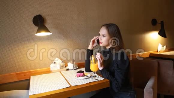 年轻女孩在电话里交谈微笑着喝着刚榨的橙汁吃着蓝莓芝士蛋糕视频的预览图