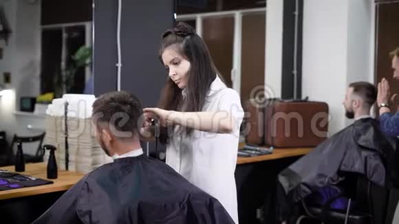 女理发师在工作男性顾客坐在椅子上其他理发师和顾客在后台场景视频的预览图
