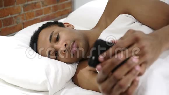 在床上使用智能手机浏览互联网的非洲男子视频的预览图
