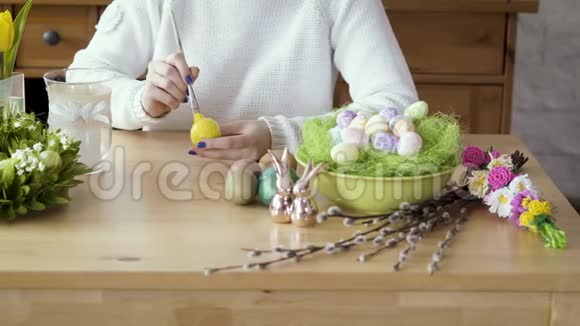 女人在桌子上画一个黄色的彩蛋上面有复活节的装饰视频的预览图