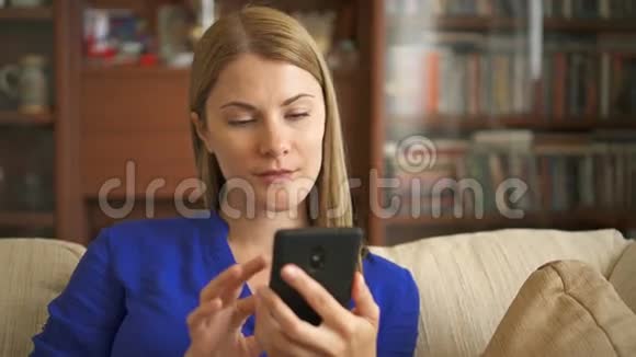 女人拿着智能手机坐在沙发上浏览互联网微笑与她的朋友交流视频的预览图