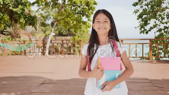 一个迷人的菲律宾女学生带着背包和书在海岸外的公园里一个女孩高兴地摆姿势举起她视频的预览图