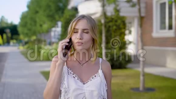 年轻的金发女郎和女朋友在手机上交谈有着天然妆容的女人走在街上视频的预览图