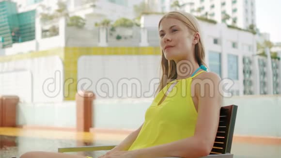 坐在游泳池附近椅子上的女人使用她的智能手机通过Skype和朋友聊天视频的预览图