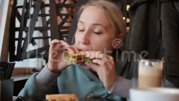 漂亮的年轻女孩在现代咖啡馆里享受美味的三明治和咖啡视频的预览图