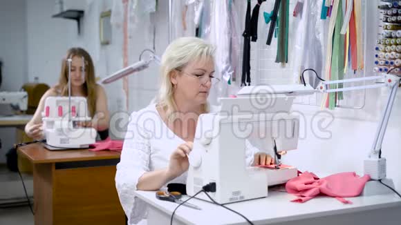 两个女人坐在桌子旁从事服装制造女人在现代机器上缝制粉红色的布视频的预览图