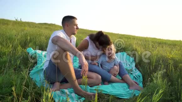 一对怀孕的夫妇和一个蹒跚学步的女儿在户外的草地上享受着悠闲的时光视频的预览图