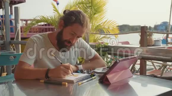男设计师在露天河边咖啡馆慢动作画草图视频的预览图
