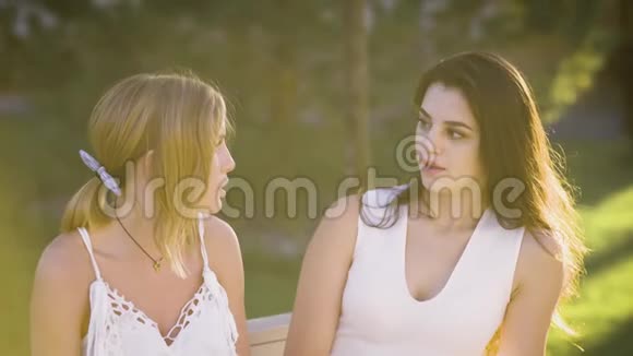 穿着白色衣服的年轻女朋友在公园的一次会议上互相交谈女人们坐在长凳上视频的预览图
