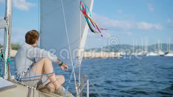 一个年轻人坐在一艘游艇的甲板上这艘游艇已经离开码头驶向海洋或大海视频的预览图