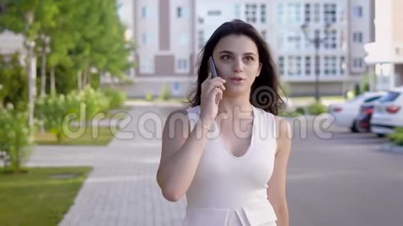 一位手里拿着手机的年轻女子在夏日的大街上自信地走着一位女士正在谈论一个视频的预览图