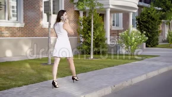 一个年轻的女人走在街上经过精英住宅这位女士正在用手机通话看起来很忙视频的预览图