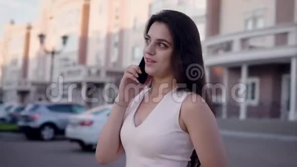 一个年轻而忙碌的女人正在和一个女朋友用手机聊天一个女士在夏天站在外面视频的预览图