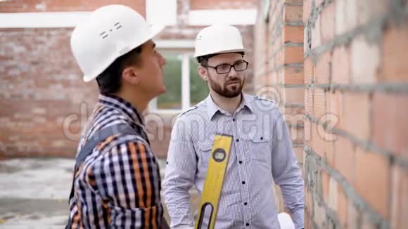 一个穿制服的成年工程师测量一个水平的砖墙一个戴防护头盔的建筑师检查数据视频的预览图