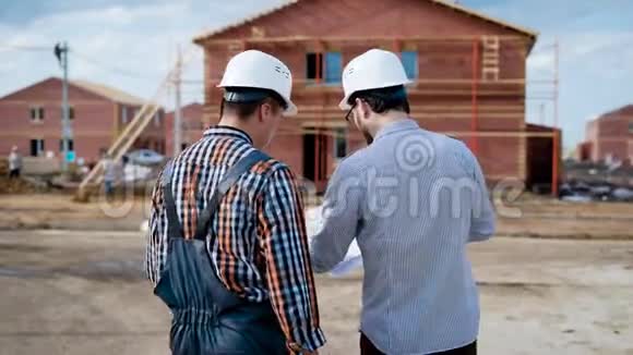 一个穿制服的建筑工人和一个戴防护头盔的成年建筑工人手里拿着一份计划视频的预览图