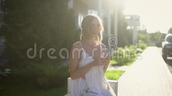 一位年轻的金发女郎用手机给朋友写信一位女士在炎热的夏天在街上拿着一部手机视频的预览图