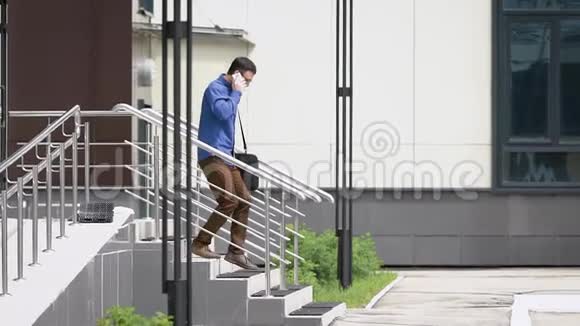 年轻的帅哥穿着蓝色休闲衬衫和棕色裤子正从大楼外面走出来在说话视频的预览图