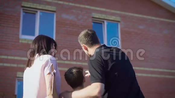 幸福的一对夫妇带着孩子看着新公寓热爱家庭在夏天阳光明媚的日子里展示男孩的现代房子母亲视频的预览图