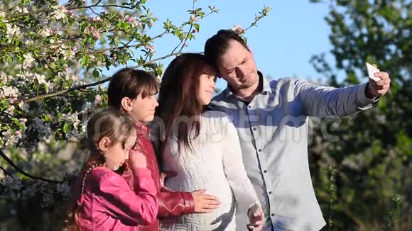 在春暖花开的公园里妈妈爸爸和女儿用电话给自己拍照视频的预览图