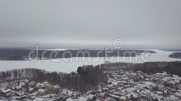 具有输电线路的电塔站在江岸上的冬村鸟瞰图无人机视图传输视频的预览图