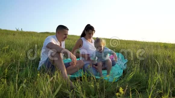 一对怀孕的夫妇和一个蹒跚学步的女儿在户外的草地上享受着悠闲的时光视频的预览图